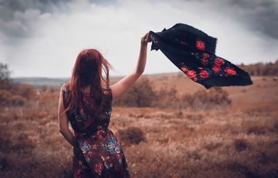 Rear view of woman waving shawl while standing on field