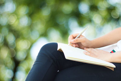 Midsection of woman writing in book while sitting outdoors