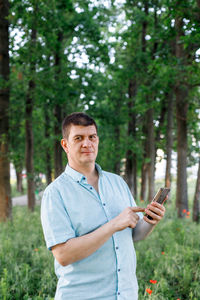 Portrait of young man using mobile phone against trees