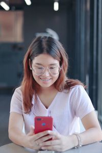 Smiling young woman using phone while sitting by table at cafe