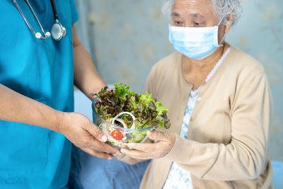 Midsection of doctor salad to patient wearing flu mask at hospital