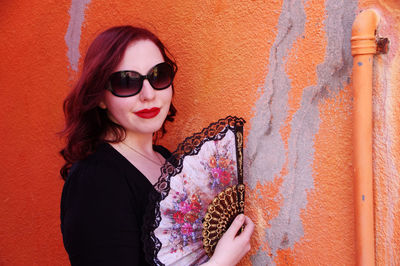Portrait of woman with folding fan by orange wall