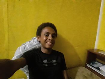 Portrait of smiling young man standing against wall at home