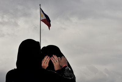 Rear view of woman in burka consoling friend against philippines flag