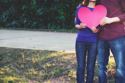 Midsection of couple holding heart shape on field