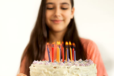 Smiling girl standing by birthday cake against wall