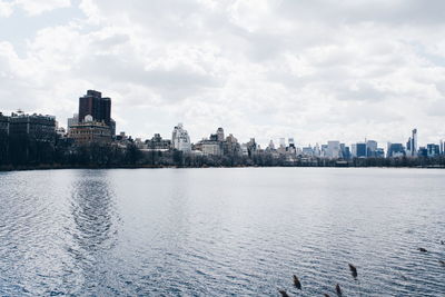 Scenic view of lake against cloudy sky in city