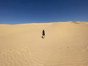 Girl on sand dune in desert against clear sky