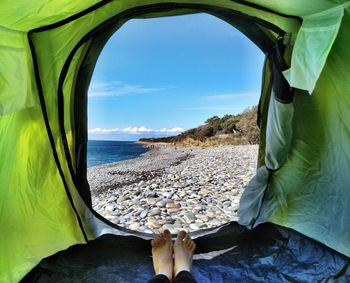 Low section of person in tent on beach against sky