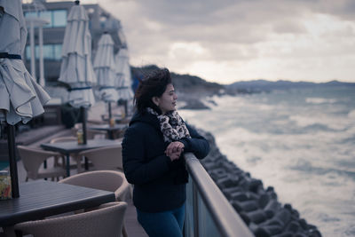 Woman standing by railing and sea against sky