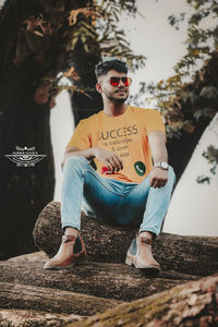 Young man sitting on chair against trees