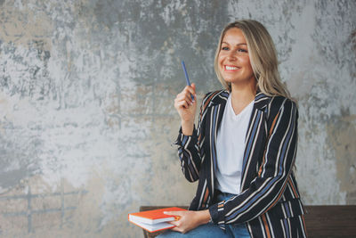 Smiling woman holding diary while sitting against wall