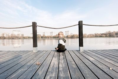 Portrait of boy sitting at pier against sky