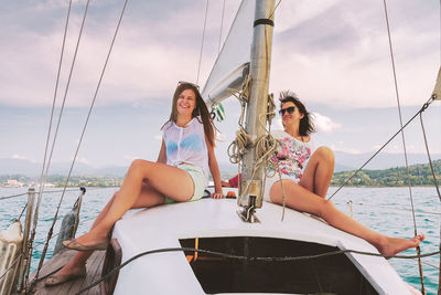 Young couple sitting on boat sailing in sea against sky