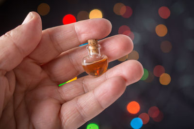 Close-up of human hand holding liquid in miniature glass bottle against illuminated lights