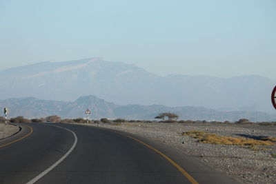 Road leading towards mountains against clear sky