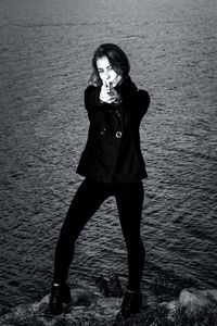 Full length portrait of young woman gesturing while standing against sea