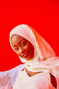 Portrait of smiling beautiful woman wearing hijab against red background