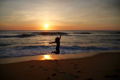 Silhouette young woman jumping at beach against sky during sunset