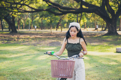 Portrait asian woman in a green casual wear walking with a bicycle looking at down in a public park