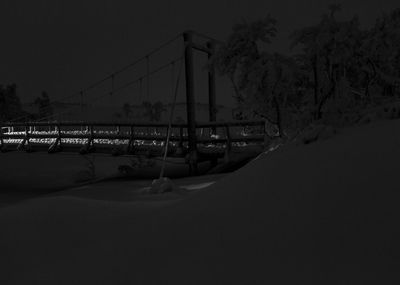 Bridge over snow covered trees against sky at night