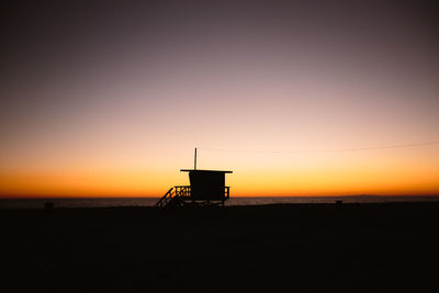 Silhouette hut by sea against sky during sunset