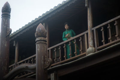 Low angle portrait of man standing by railing against building