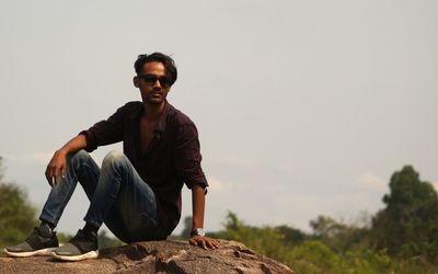 Young man sitting on rock against clear sky