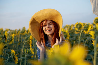 Portrait of young woman wearing hat standing on field against sky