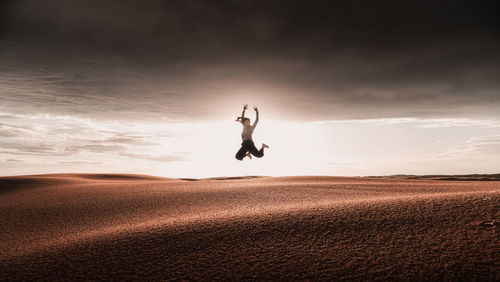 Man jumping on sand against sky