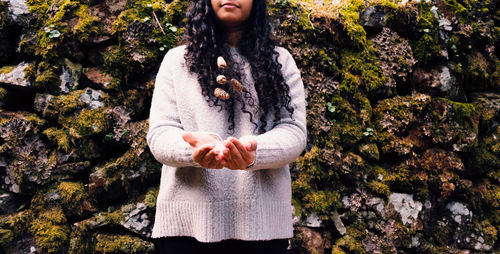 Midsection of woman catching pine cones against stone wall