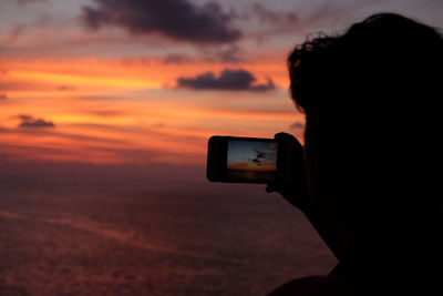 Silhouette person photographing camera against sky during sunset