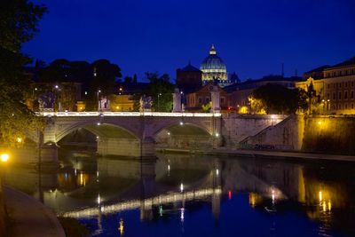 Illuminated bridge over river against buildings at night