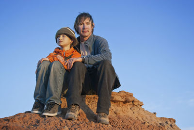 Portrait of father and son sitting on mountain against clear sky