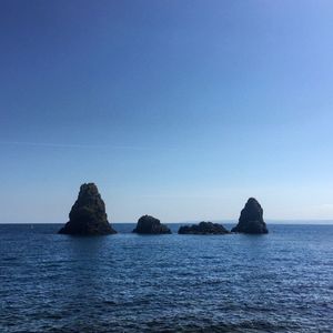 Rocks in sea against clear blue sky