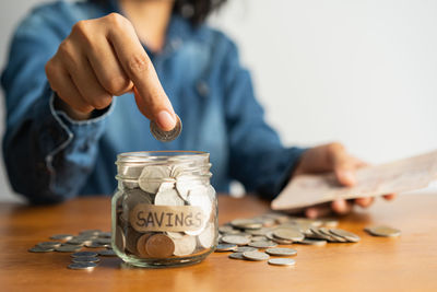 Close-up of hand holding coins in jar on table