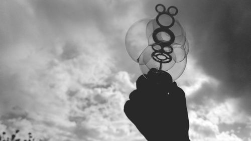 Cropped hand holding bubble wand against sky