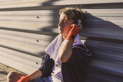 Boy listening to music through headphones while sitting against wall