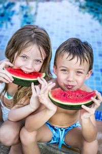 Cute siblings having watermelon against swimming pool