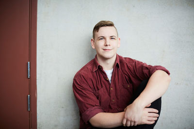 Portrait of young male student sitting against wall in university