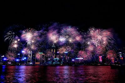 Firework display over sea against sky at night