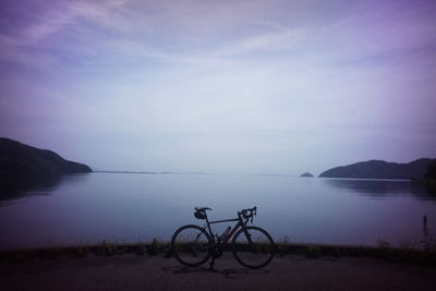 Bicycle by lake against sky at dusk