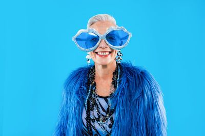 Portrait of young woman wearing sunglasses against blue background