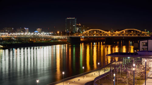 Illuminated bridge over river in city against sky at night