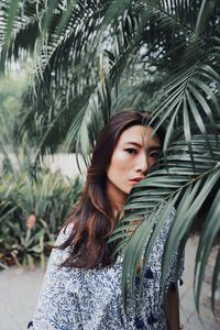 Portrait of serious young woman standing by plants in park