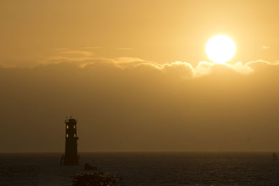 Lighthouse amidst sea against sky during sunset