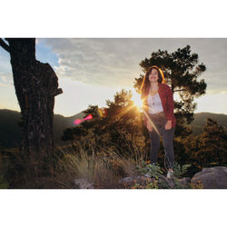 Portrait of young woman standing on field at sunset