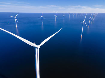 Wind turbines in sea against blue sky
