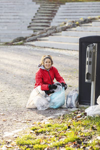 Portrait of female volunteer crouching with plastic waste by garbage can