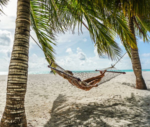 Mid adult woman relaxing on hammock at beach against sky